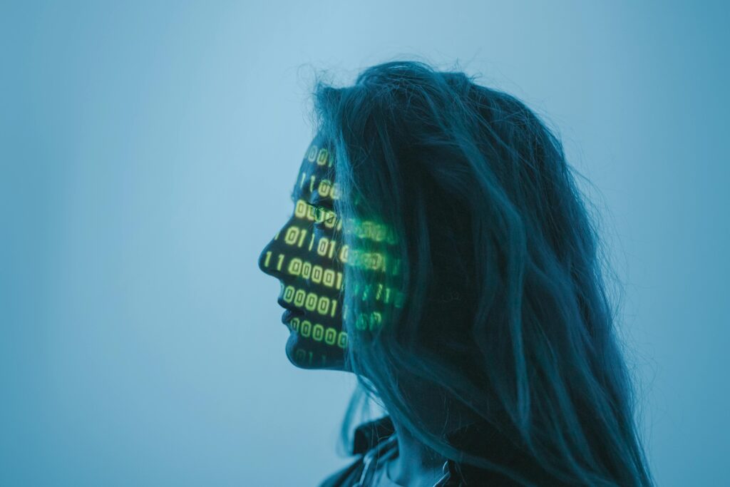 Close up view of a woman's face in dark lighting, with lines of software code projected on her face. 
